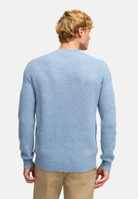Hellblauer, gerippter Strickpullover mit langen Ärmeln und Rundhalsausschnitt. Verfügt über einen strukturierten Stoff und einen figurbetonten Saum. Getragen mit beigen Hosen.