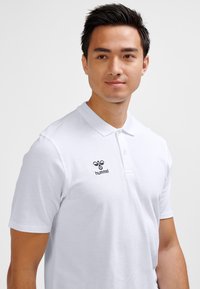 Witte poloshirt van katoen met een klassieke kraag en een Hummel-logo aan de linkerkant. Korte mouwen, gladde textuur.