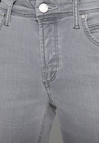 Vaqueros de mezclilla gris con un diseño clásico de cinco bolsillos, cierre de cremallera y un botón metálico con grabado de la marca. Tejido de textura suave.