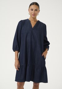 Tmavomodré, džínsové šaty s výstrihom do V, nariasenými rukávmi a vrstveným, volánovým lemom. Obsahujú bočné vrecká a majú voľný strih.