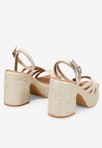 Sandalias de plataforma beige con tiras, con un tacón de bloque de yute trenzado y una correa de tobillo ajustable. Plantilla lisa en tono marrón claro y detalles texturizados.
