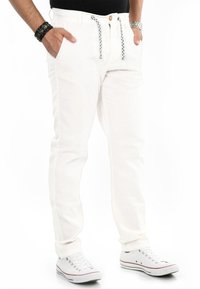 Weiße Hose mit Kordelzugbund, seitlichen Taschen und einer subtilen Textur. Kombiniert mit weißen Sneakern und einem schwarzen Shirt.