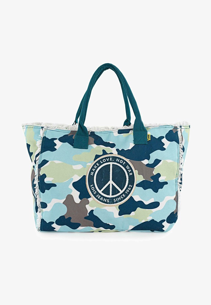 Bolsa de tote con estampado de camuflaje en azul claro, verde y gris, con flecos decorativos y un parche central en forma de símbolo de paz con texto. Material de algodón.