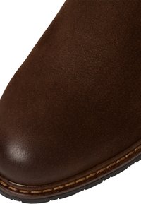 Bottine en cuir marron avec une texture lisse, bout rond et coutures visibles près de la semelle. Semelle en caoutchouc épaisse pour une durabilité accrue.
