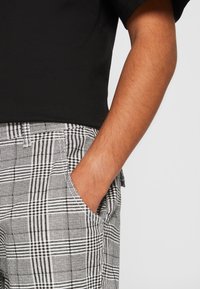 Zwarte shirt met korte mouwen gecombineerd met grijs-witte geruite broek met een ruitpatroon en zijzakken.