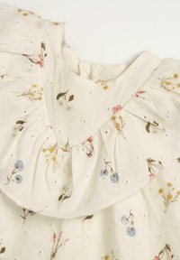 Robe blanche à imprimé floral, avec un col volanté et des détails en broderie ajourée. Tissu doux avec des fleurs pastel et des accents verts.
