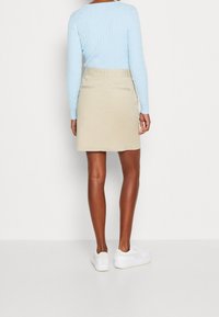 Ljusblå kabelstickad tröja, beige kjol med bakfickor, bärs tillsammans med vita sneakers, vilket visar en avslappnad, figurnära silhuett.