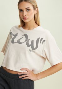 Camiseta corta de color rosa claro con un estampado gráfico gris que dice "FREDDY" en un estilo fluido. Mangas cortas y cuello redondo; hecha de tela de algodón.