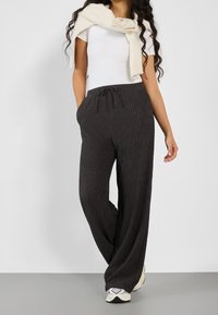 Donkergrijze geribde wijde broek met een elastische tailleband en trekkoord, gecombineerd met een aansluitend wit t-shirt en een wit sweatshirt dat om de schouders is geknoopt.