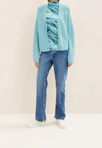 Cardigan lavorato a maglia di un blu chiaro, aderente sulle spalle, abbinato a un dolcevita turchese a spirale e jeans blu chiaro. Sneakers bianche completano il look.