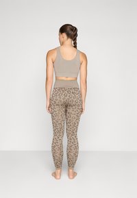 Beige sports-BH med en kort design kombinert med høyt liv leggings med et lyse leopardmønster på en beige bakgrunn.