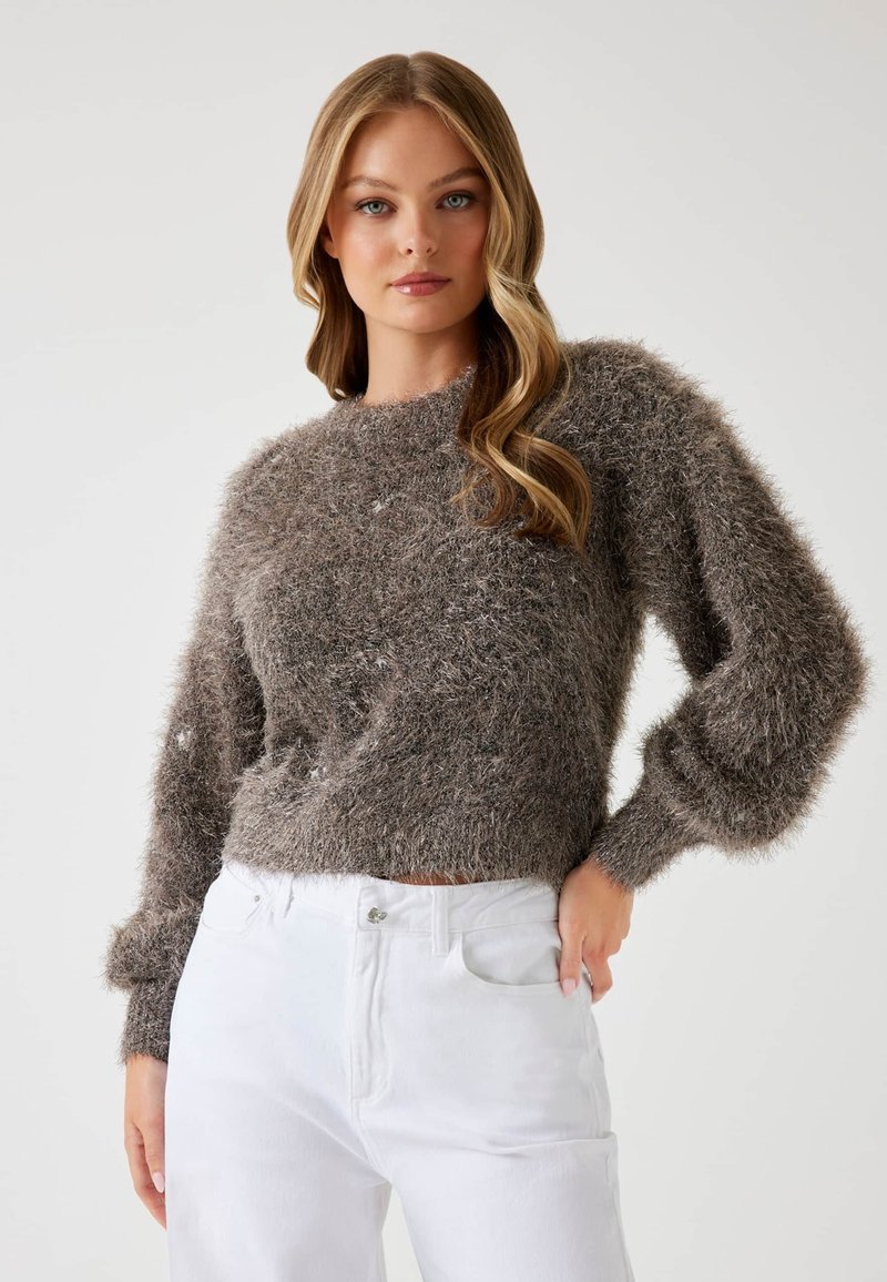 Maglione marrone peloso con collo rotondo, maniche lunghe a sbuffo e finiture a coste, abbinato a jeans bianchi a vita alta. Aspetto morbido e dalla texture ricca.