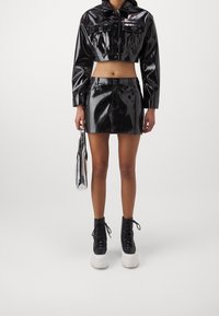 Black glossy cropped jacket with matching mini skirt, paired with platform black boots and a silver clutch bag. Smooth texture and fitted design.