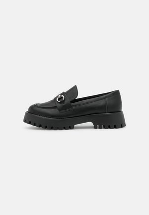 Mocassin en cuir noir avec semelle crantée épaisse et détail boucle en métal argenté sur le dessus, vue de profil sur fond blanc.