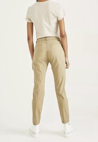 Beige katoenen broeken met een getailleerde pasvorm, lichte tapering, twee achterzakken en een gladde structuur, gecombineerd met witte sneakers.