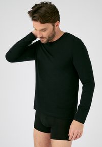 Zwarte langemouwen shirt gemaakt van zachte stof, met een ronde halslijn en een getailleerde pasvorm, gecombineerd met zwarte boxershorts, weergegeven tegen een effen achtergrond.