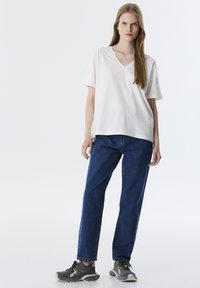 Weißes V-Ausschnitt-T-Shirt, entspannter Schnitt, kombiniert mit blauen Jeans im klassischen Schnitt. Dazu graue Sneakers, minimalistischem Design und Farben.