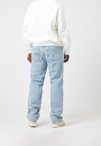 Ljusblå denimjeans med en avslappnad passform, med en klassisk femfickdesign och subtilt urtvättad textur, kombinerat med en vit sweatshirt.