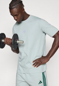 Gaiši zilais sporta t-krekls ar īsām piedurknēm, uz krūtīm neliels lavandas tonī logo, kopā ar atbilstošām biksēm un svaru.