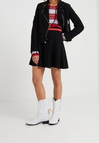 Black suede jacket over a red and white striped sweater, paired with a black flared skirt and white cowboy boots with contrasting black soles.