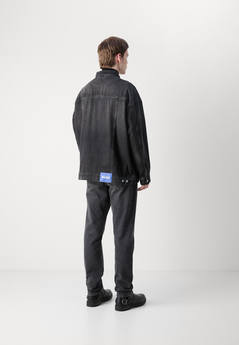 Czarna kurtka dżinsowa o luźnym kroju, z niebieską metką "HUGO" oraz pasującymi ciemnymi dżinsami. Gładka tekstura i minimalne detale z metalu.