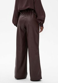 Brązowe skórzane spodnie wide-leg o gładkiej teksturze, z elastycznym paskiem w talii i minimalnym wykończeniem.