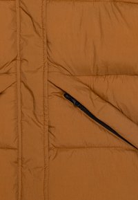 Sezione di giacca puffer marrone con texture trapuntata. Presenta una tasca laterale con zip e cuciture a vista. Tessuto liscio e leggero.