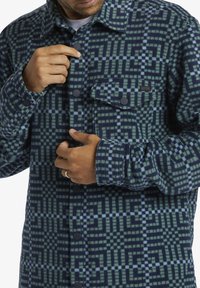 Knopenoverhemd van flanel met een geometrisch groen en marineblauw patroon, gemaakt van zachte stof met zwarte drukknoopsluitingen en een borstzak.