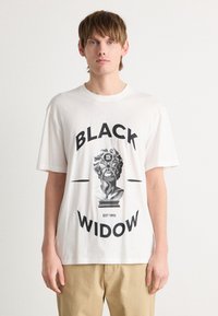 Hvit bomulls t-skjorte med grafisk trykk av en statue og ordene "BLACK WIDOW" i fete svarte bokstaver under. Avslappet passform.