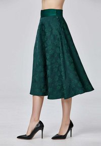 Jupe midi à motif floral vert avec une large taille, une coupe évasée et une texture lisse, associée à des escarpins noirs à talons aiguilles.
