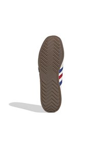 Suela de goma marrón de una zapatilla Adidas con patrón de banda de rodadura en zigzag, mostrando la parte superior blanca parcial con rayas azules y rojas.