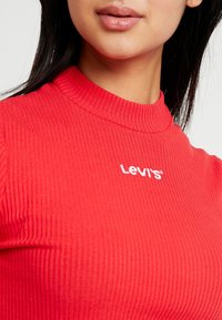 Červený žebrovaný rolák s krátkými rukávy, na přední straně s vyšitým bílým logem "Levi's". Hladká textura, přiléhavý design.