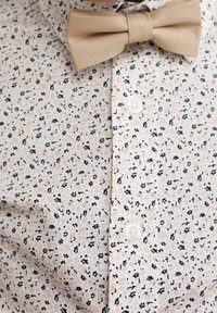 Camicia a maniche corte con un motivo floreale beige, nero e marrone chiaro. Presenta un colletto a punta e un papillon in satin beige.