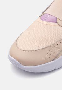 Light beige sneaker featuring a textured mesh upper, a lavender accent, and white rubber sole with perforated detail.