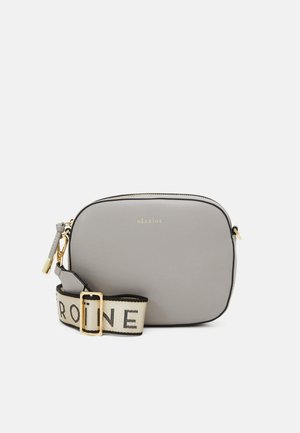 Szara skórzana torba na ramię o gładkiej teksturze, złotym okuciu i białym pasku z napisem "HÉROÏNE" w czarnym kolorze. Zamek błyskawiczny. Prostokątny kształt.