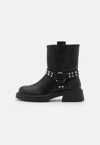 Bottes noires en cuir à cheville avec un talon épais, ornées d'une sangle décorative avec des clous en argent et un anneau en métal.