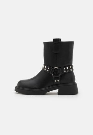 Black leather ankle boots with a chunky heel, adorned with a decorative strap featuring silver studs and a metal ring.