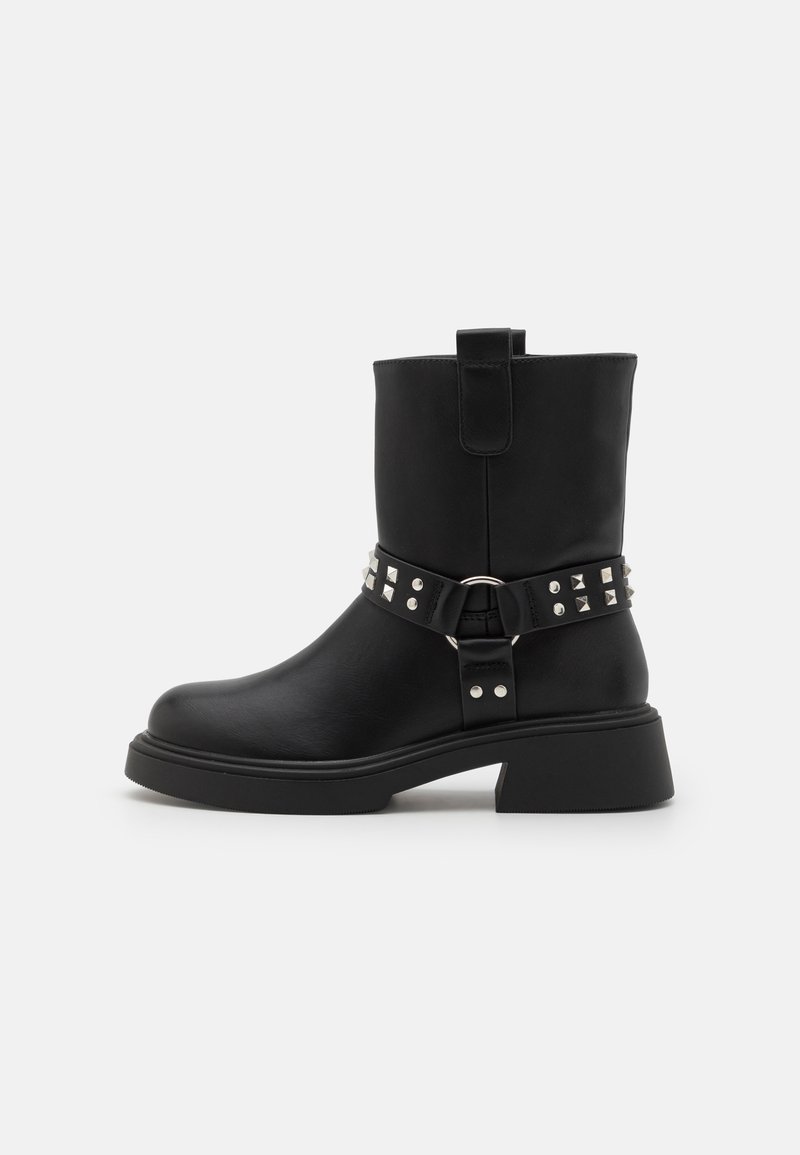 Botas de ankle em couro preto com um salto grosso, adornadas com uma faixa decorativa featuring tachas prateadas e um anel de metal.