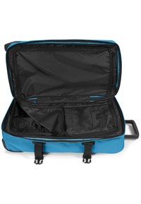 Valigia a ruote in tessuto blu con un ampio scomparto aperto, interno nero, molteplici tasche e doppie cinghie con fibbie in plastica per il fissaggio.