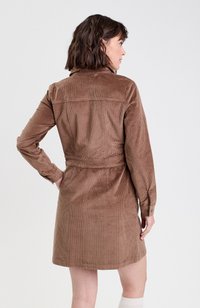 Robe en velours côtelé marron avec des manches longues, taille ceinturée et détail de yoke au dos. Présente une texture côtelée verticale et une longueur mi-thigh.