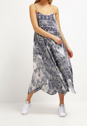 Robe maxi en bleu marine et blanc avec des motifs géométriques et abstraits, fabriquée en tissu léger, dotée de bretelles spaghetti et de fentes sur les côtés.