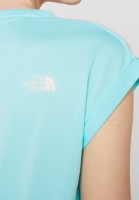 T-shirt bleu clair à manches courtes, fabriqué en tissu lisse. Présente un logo blanc de The North Face dans le dos, près de l'encolure.