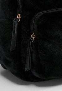 Tissu en peluche noir doux avec deux languettes de fermeture éclair noires fixées à des curseurs dorés sur un sac ou une pochette.
