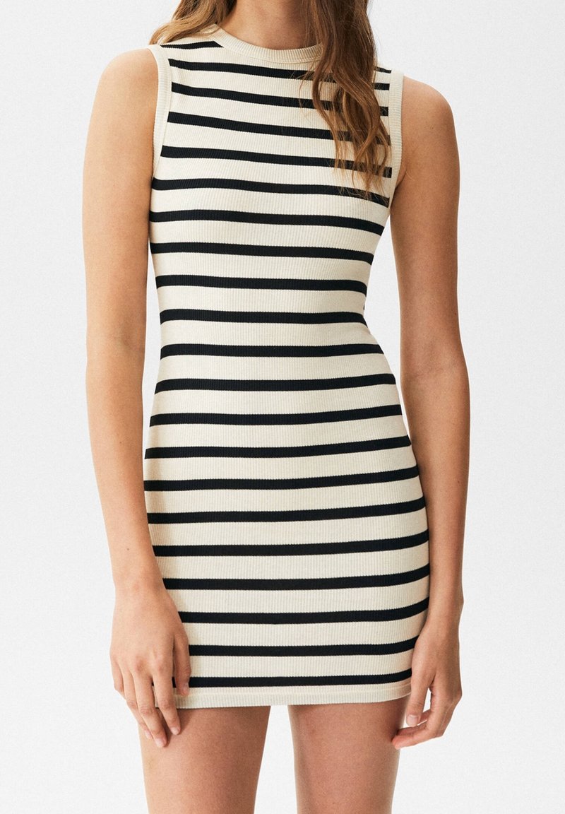 Robe sans manches côtelée avec des rayures horizontales noires et crème, silhouette ajustée, portée par une personne aux longs cheveux ondulés.