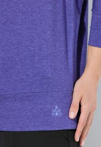 Paarse, gemêleerde shirt met driekwart mouwen, een relaxte pasvorm en een klein logo aan de onderrand. Zachte textuur, lichtgewicht stof.
