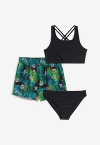 Top da bagno nero con spalline incrociate, slip bikini neri e pantaloni da bagno a stampa floreale multicolore con motivi di foglie tropicali.