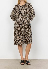 Vaaleanruskea polvipituinen mekko leopardikuvioin, jossa on väljä leikkaus, lyhyet hihat ja pyöreä pääntie. Yhdistetty mustiin korkokenkiin.