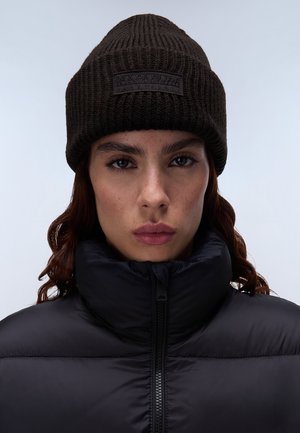 Berretto lavorato a maglia di colore marrone scuro con texture a costine, dotato di un patch logo nero. Indossato con un giubbotto imbottito nero con collo alto.
