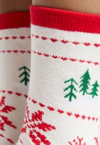 Calze lavorate a maglia rosse e bianche con motivi di alberi verdi e fiocchi di neve, dotate di un polsino rigato rosso. Morbida texture e design stagionale.