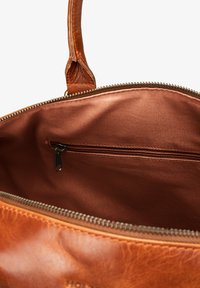 Leather handbag interior in rich brown, featuring a smooth satin lining and a zippered pocket for organizing essentials.